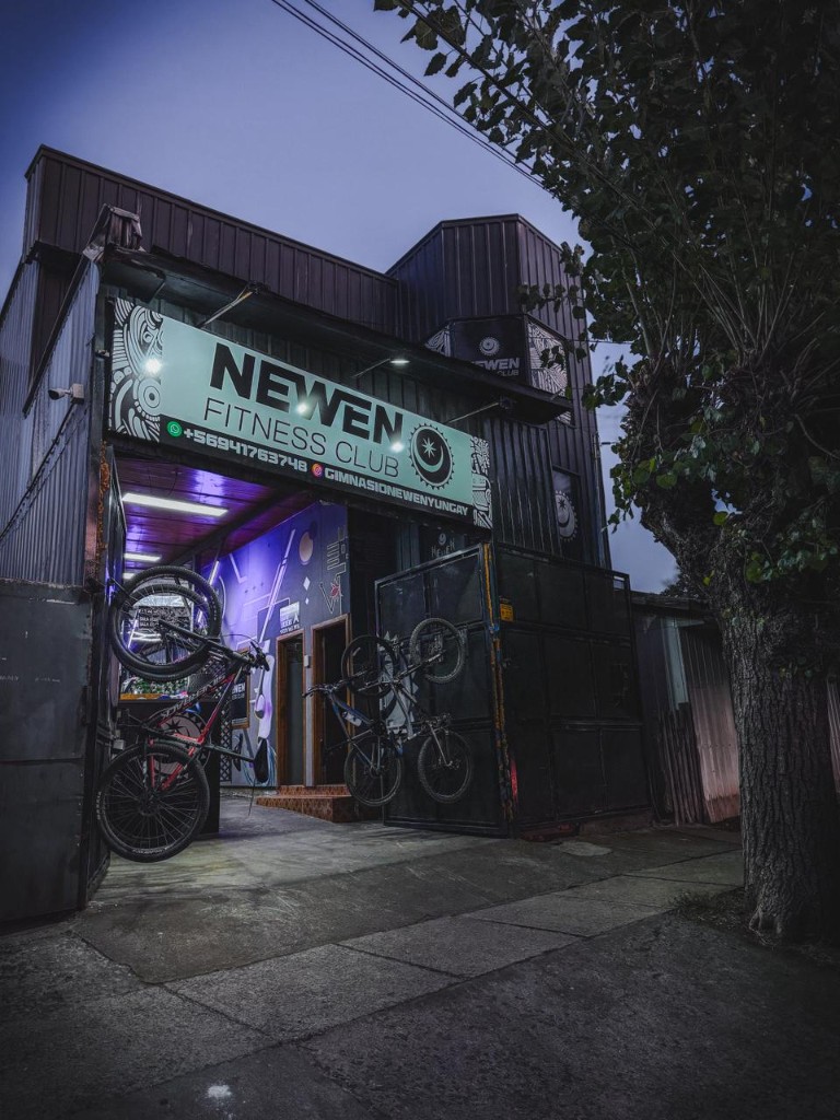 Fachada de Newen Fitness Club al anochecer, con el letrero e ingreso a Germania 473, Yungay